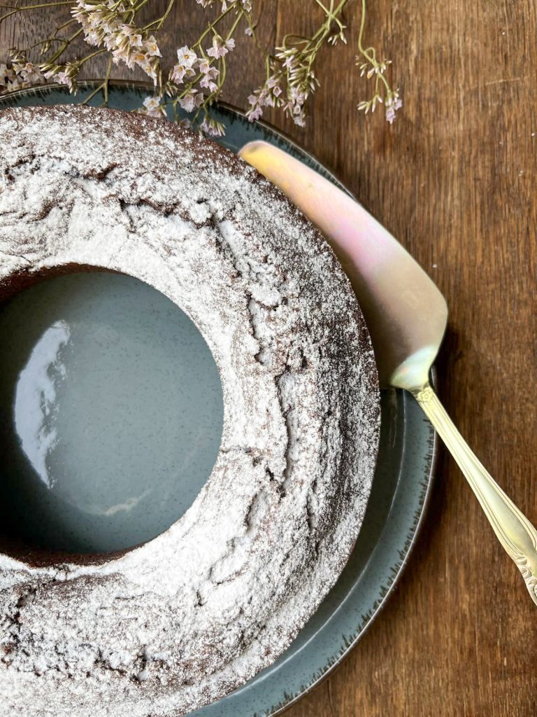 Allergy friendly chocolate cake on a blue plate with a golden cake slice and dried flowers