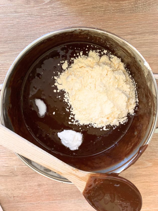 Flour, salt and baking powder in chocolate cake batter in saucepan with a wooden spoon  on a wood finish surface