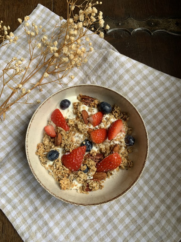 Homemade honey granola served with Greek Yoghurt and berries on a checked cloth with dried flowers