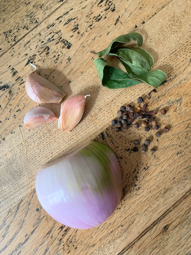 onion, garlic, bay leaves, peppercorns and cloves on a wooden table