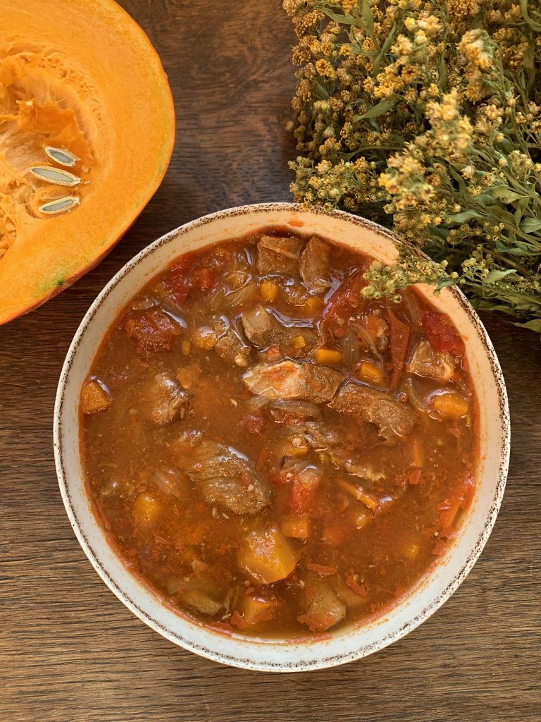 Autumn pork goulash stew recipe with an onion squash and dried flowers on a wooden surface
