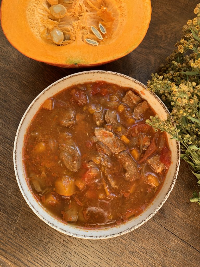 Autumn Pork Goulash Stew in a bowl with onion squash on a wooded surface