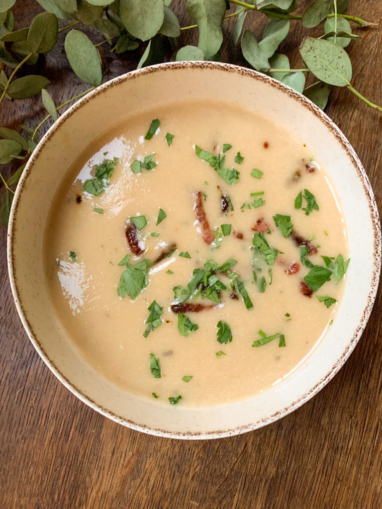 Creamy white bean soup with roasted garlic and bacon seen from above on a wooden table with eucalyptus