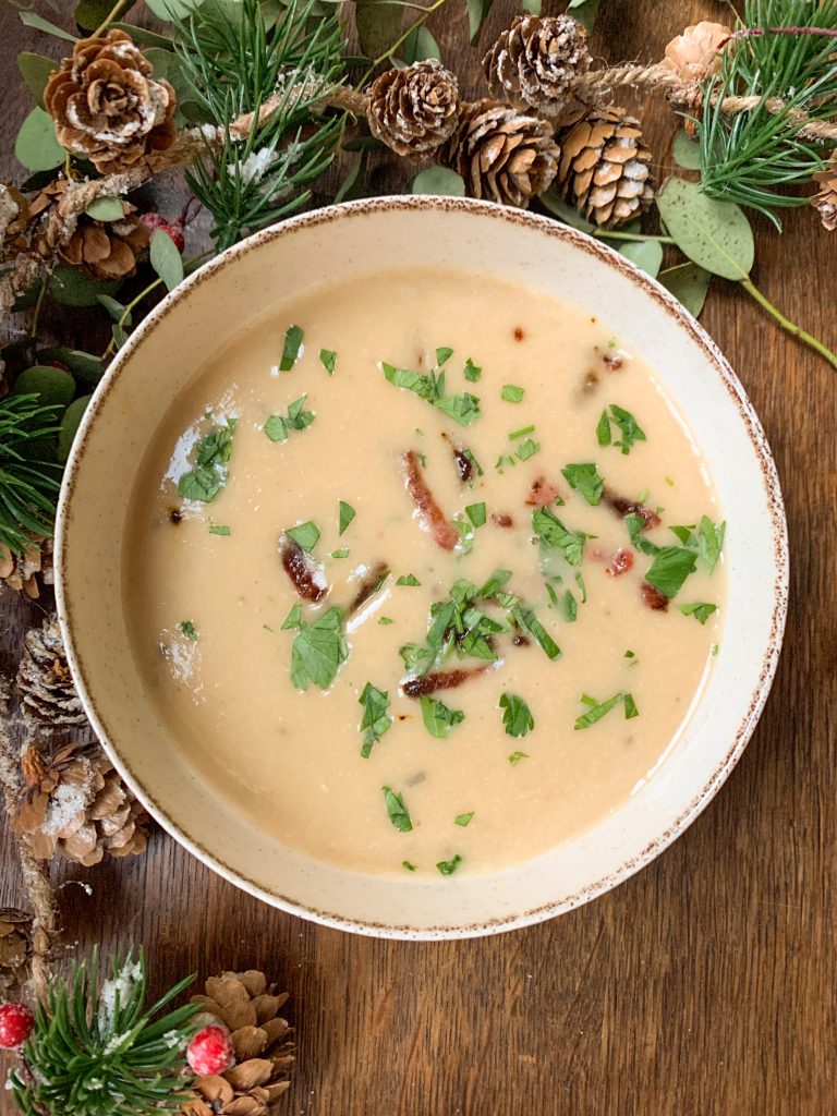 Creamy white bean soup with roasted garlic and bacon on a wooden table with christmas garland