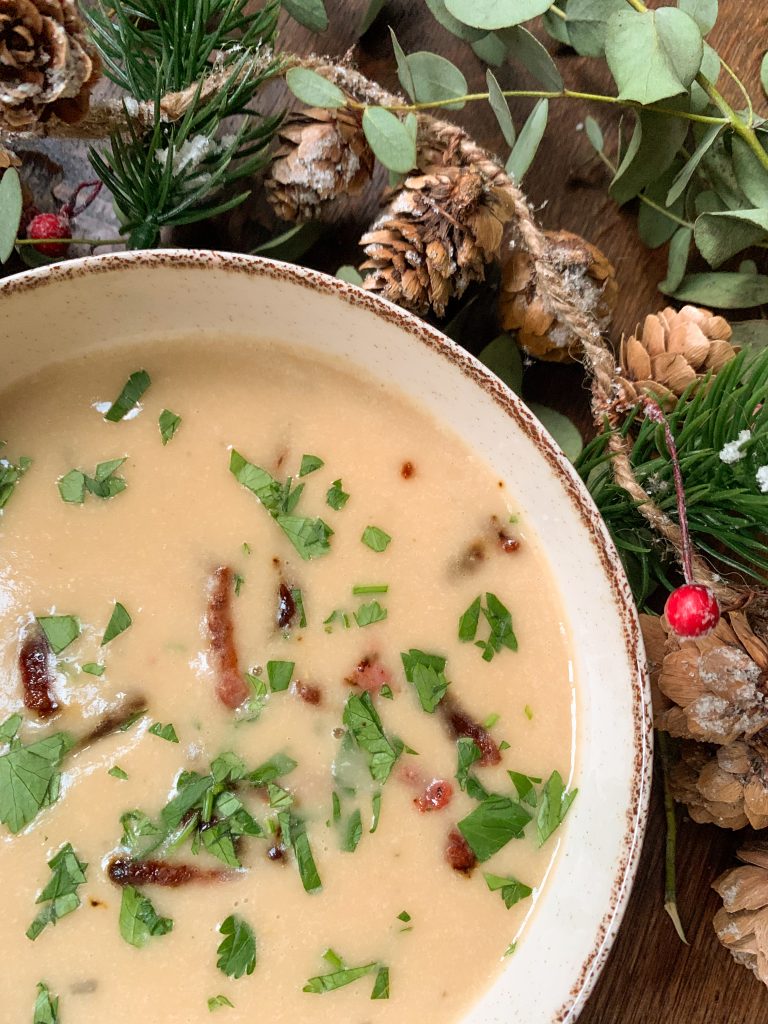 Creamy white bean soup with roasted garlic and bacon on a wooden table with christmas garland
