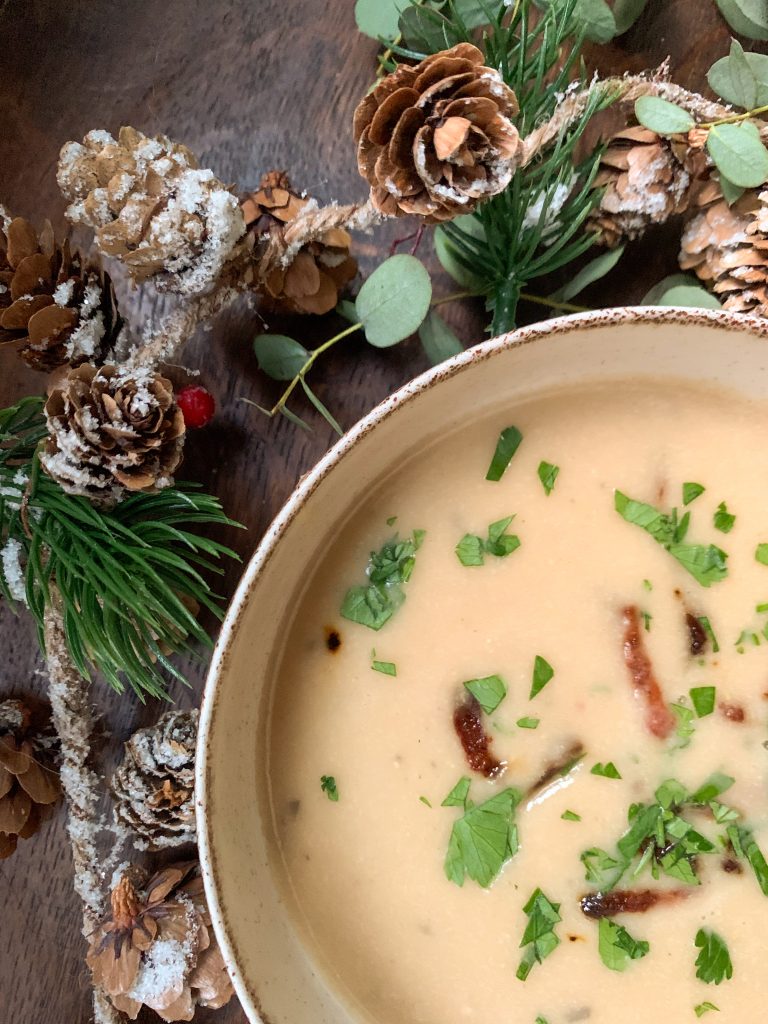 Creamy white bean soup with roasted garlic and bacon on a wooden table with christmas garland