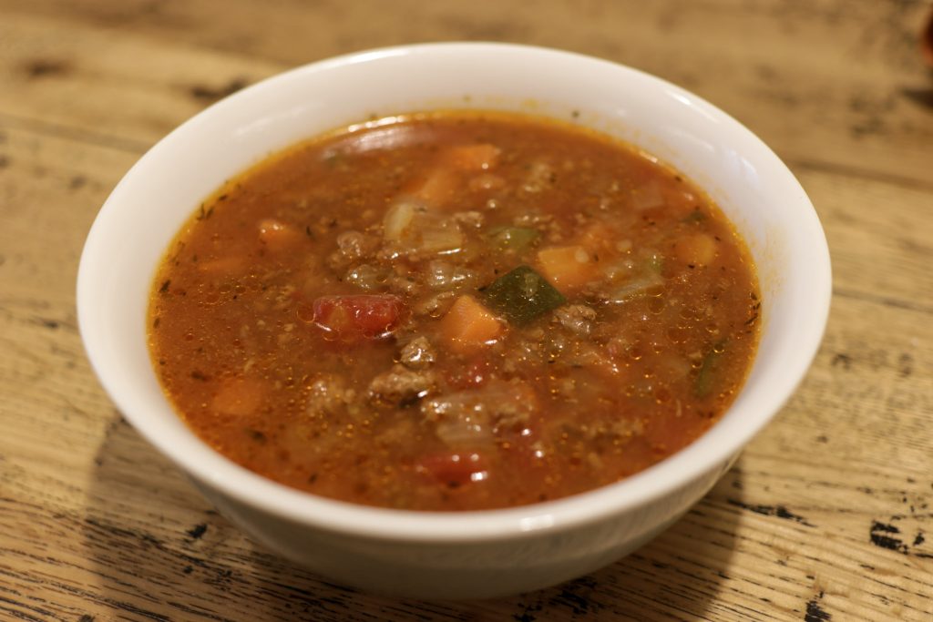 Minced beef and tomato soup in a white bowl on a wooden table