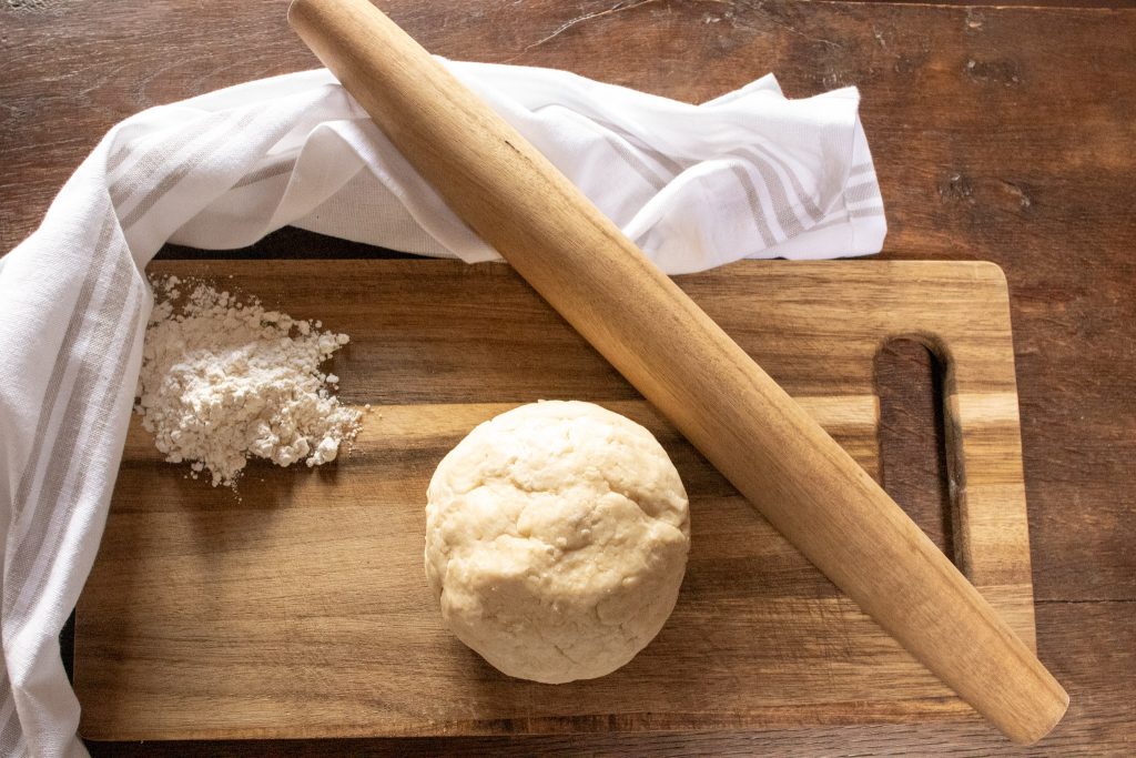 Sourdough discard pastry crust in a ball on a wooden board with flour and a rolling pin