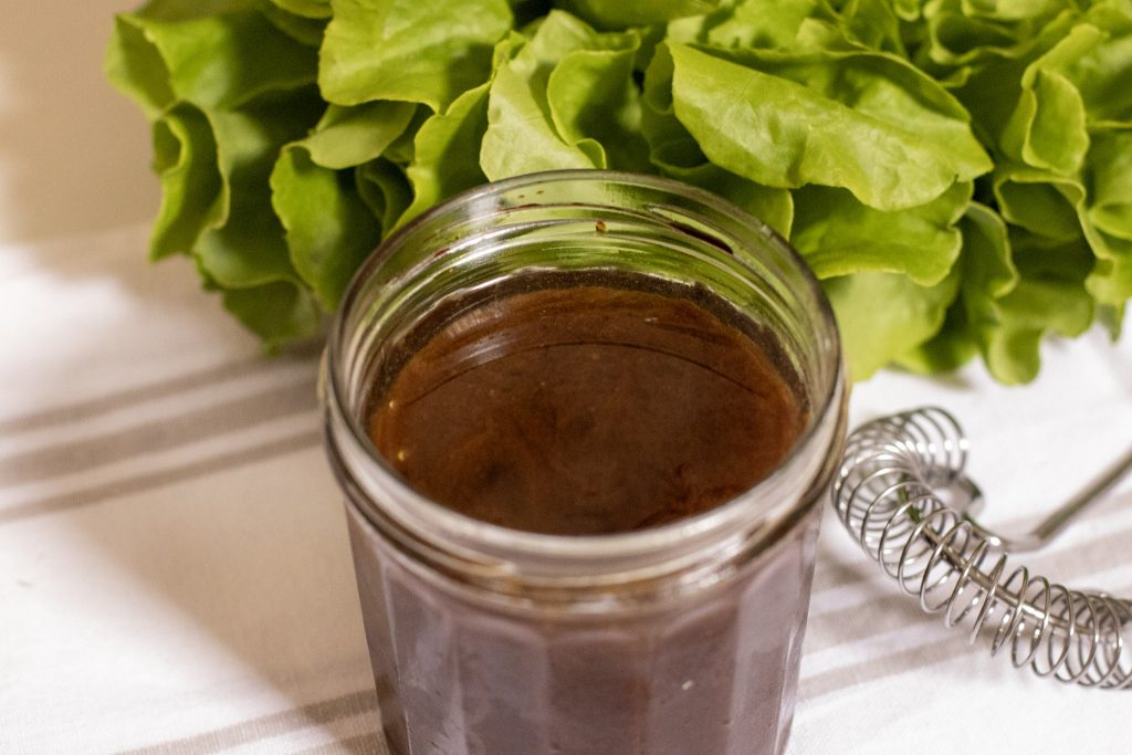 Asian Style Balsamic Salad Dressing in a jam jar with a lettuce in back ground and whisk 