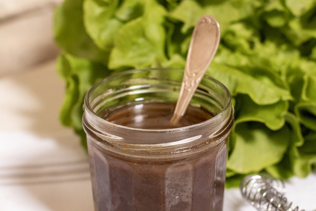 Asian Style Balsamic Salad Dressing in a jam jar with a lettuce in back ground and spoon in jar