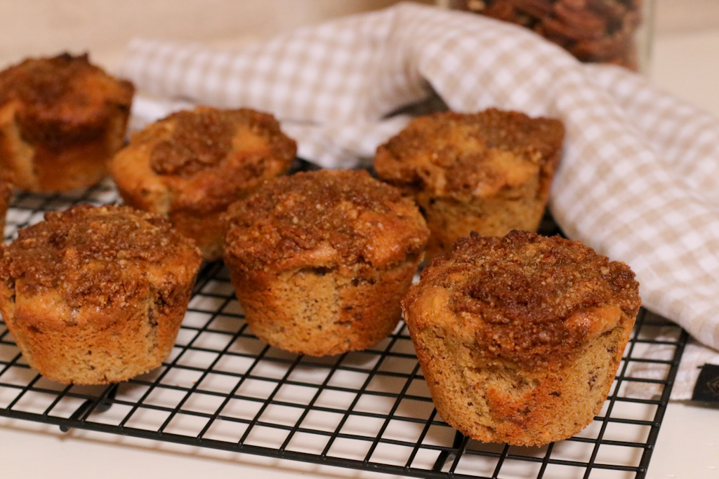 Whole wheat maple and pecan muffins on a black cooling rack with a checked tea towel behind