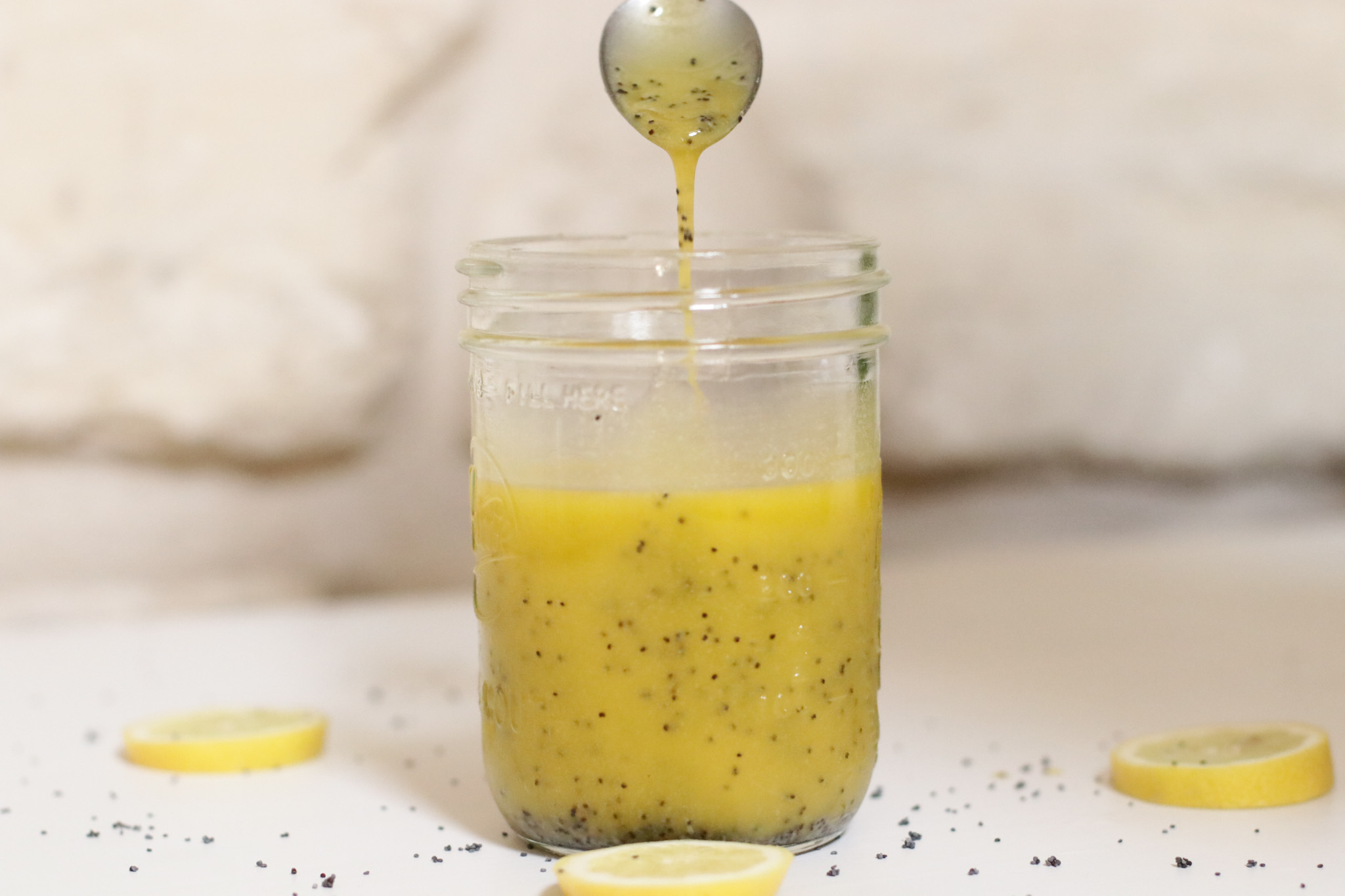 Lemon and poppy seed dressing in a mason jar with dressing dribbling from a spoon