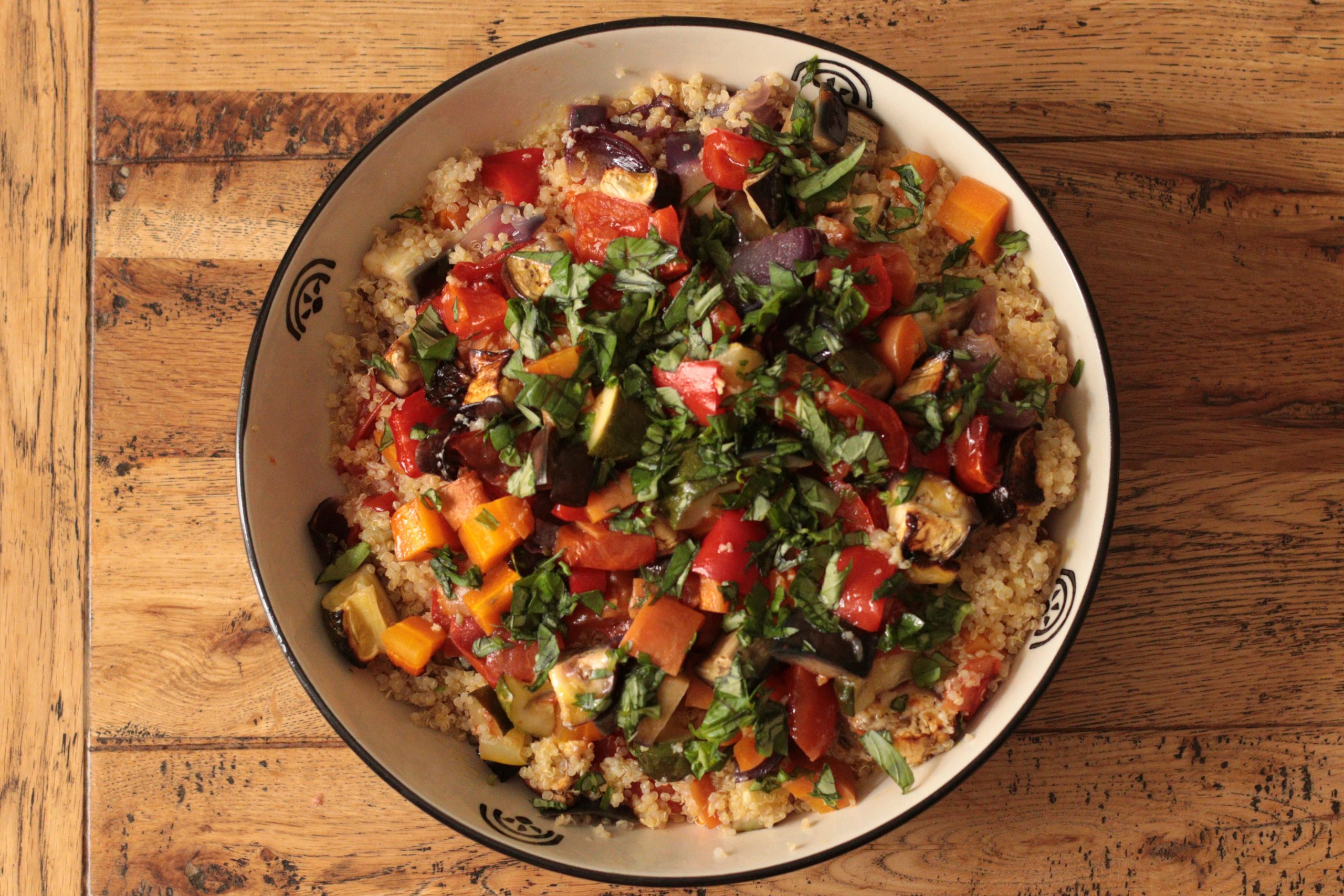Quinoa salad with roasted vegetables served in a blue bowl, topped with fresh herbs