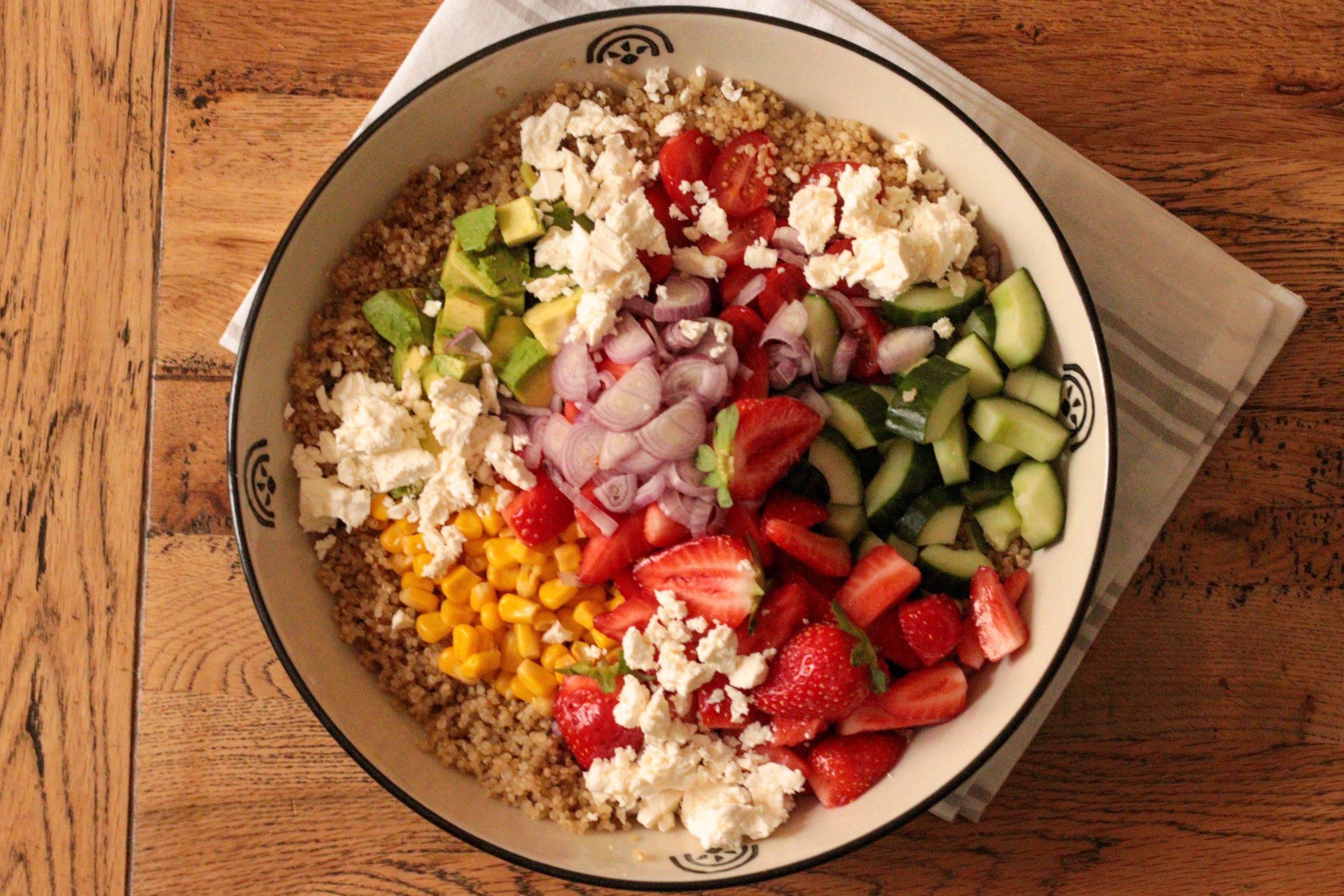 overhead of quinoa salad recipe with strawberries, fresh veggies and feta before tossing